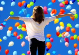 Montage photo d'une femme de dos avec les bras tendus sur les côtés avec un fond avec des ballons de baudruche.