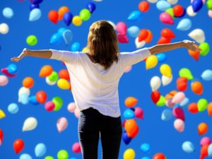 Montage photo d'une femme de dos avec les bras tendus sur les côtés avec un fond avec des ballons de baudruche.